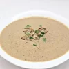 Un bol alb cu supa crema de ciuperci decorat cu ciuperci deasupra si verdeata