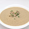 Un bol alb cu supa crema de ciuperci decorat cu ciuperci deasupra si verdeata